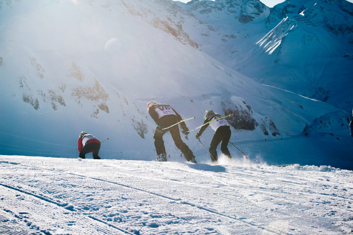 Drei Skifahrer fahren über eine Kuppe